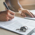 close up hands businessman signing leasing home documents have apartment keys
