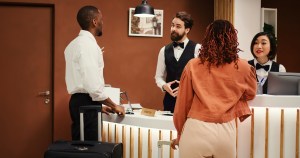 hotel manager handing arriving visitors booking reservation file receptionists check business travelling guests being assisted by helpful concierge staff coworkers inside reception lobby